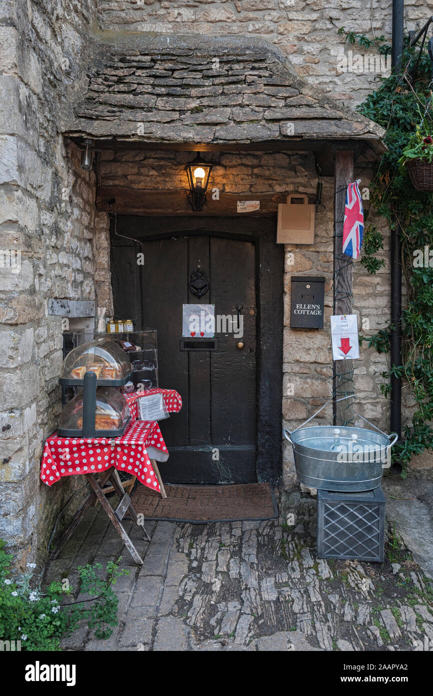 Bella facciata di vecchio cottage in pietra con tavolo da tavolo che vende torte fatte in casa nel pittoresco villaggio di Castello Combe, Chippenham, Cotswolds Foto Stock