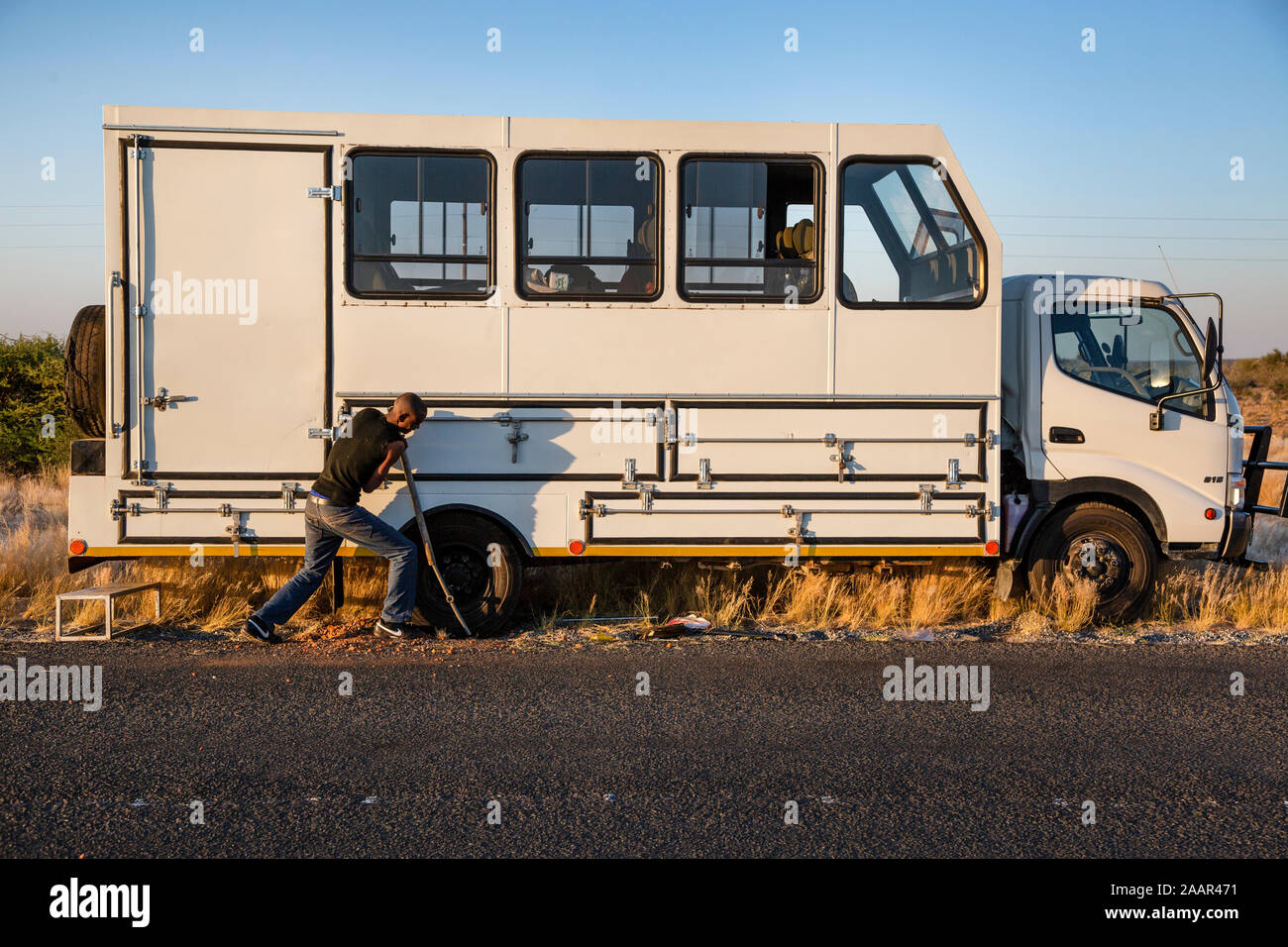 Un autista di riparazione di una ruota in un autobus turistico su una strada in Namibia, Africa Foto Stock