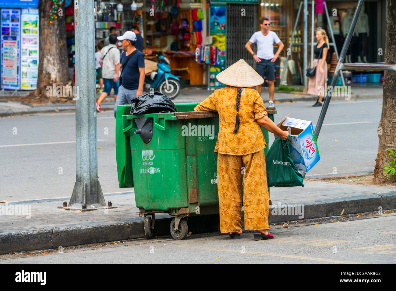 Hanoi, Vietnam - XII Ottobre 2019: una donna asiatica trasporta rifiuti e immondizie fuori del verde del bidone dei rifiuti nelle strade di Hanoi, Vietnam Asia Foto Stock
