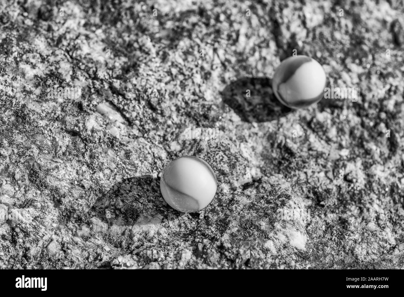 Marmi in vetro bianco e nero su superficie ruvida in pietra. Per qualcosa perso, salute mentale, perdere i vostri marmi, sfere astratte, sogni, Biden & marmi. Foto Stock