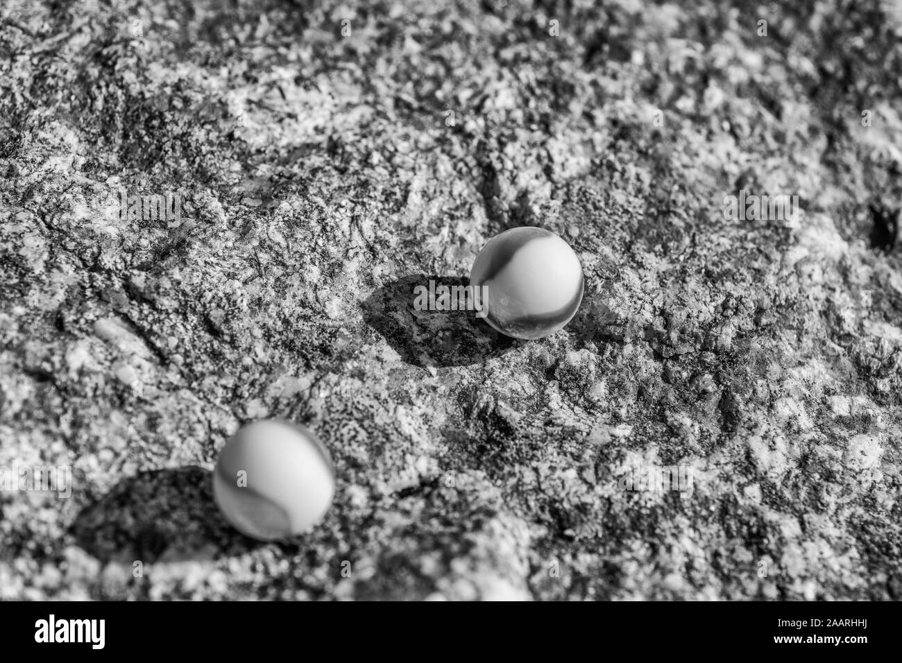 Marmi in vetro bianco e nero su superficie ruvida in pietra. Per qualcosa perso, salute mentale, perdere i vostri marmi, sfere astratte, sogni, Biden & marmi. Foto Stock