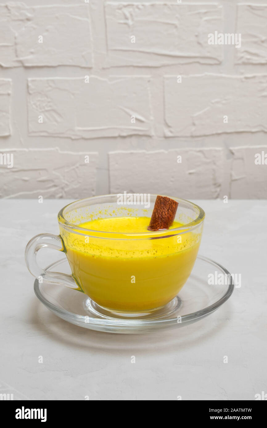 Tradizionale bevanda indiana golden curcuma latte in un bicchiere di vetro con la stecca di cannella sul folle tabella di calcestruzzo Foto Stock