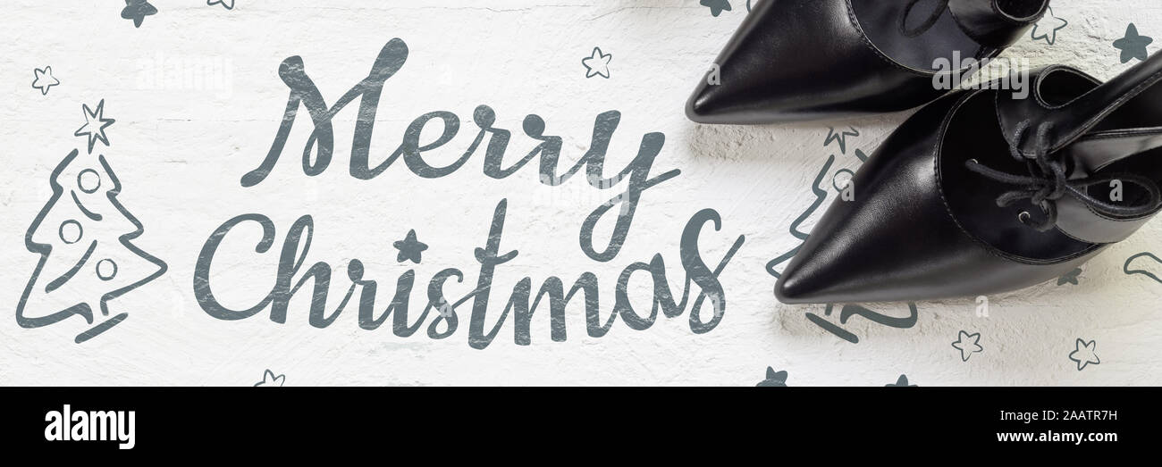 Buon Natale e la stagione invernale moda banner web Concetto di sfondo. Piatto nero laici tacco alto scarpe e mini albero di natale su grunge di legno bianco b Foto Stock