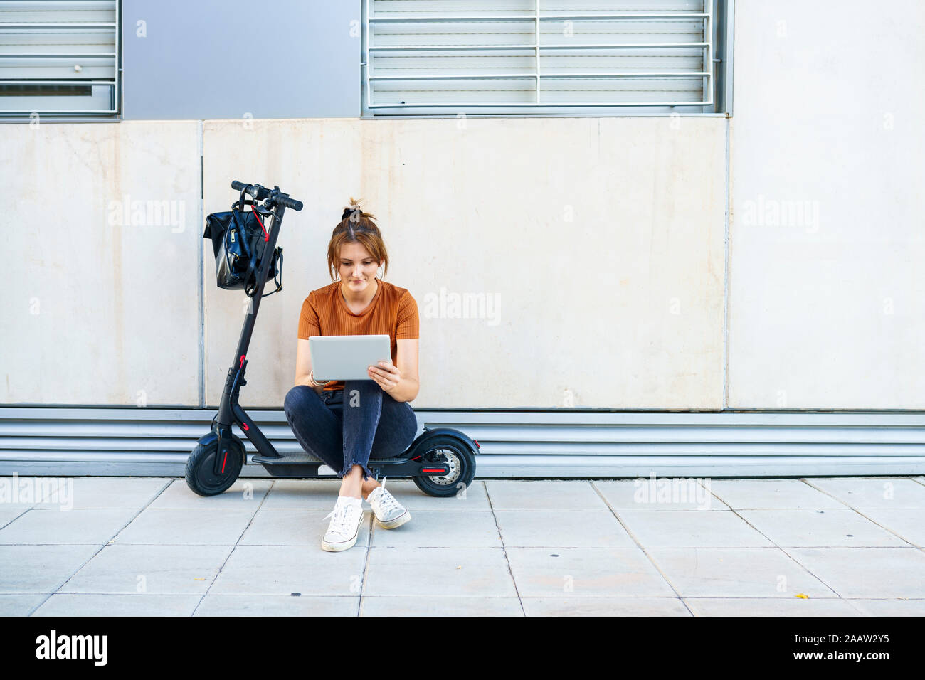 Ritratto di donna seduta su scooter elettrico utilizzando tavoletta digitale Foto Stock