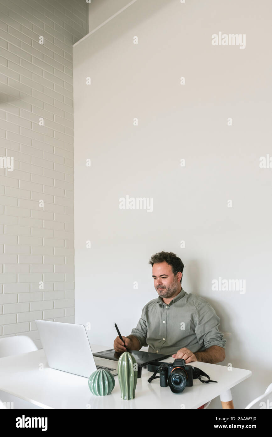 Ritratto di uomo seduto a tavola lavorando sulla tavoletta grafica e il computer portatile Foto Stock