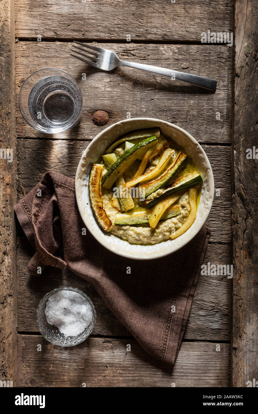 Direttamente sopra il colpo di hummus con zucchine fritte servite nella ciotola con acqua potabile sul tavolo di legno Foto Stock