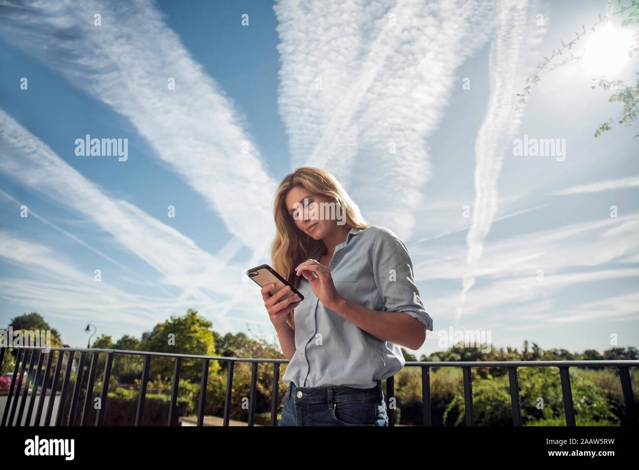 Donna texting sullo smartphone, in piedi sul balcone Foto Stock