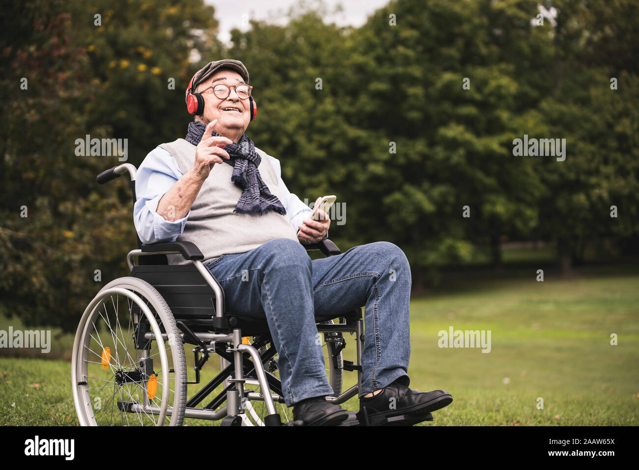 Ritratto di felice senior uomo seduto nella sedia ascoltando musica con lo smartphone e le cuffie Foto Stock