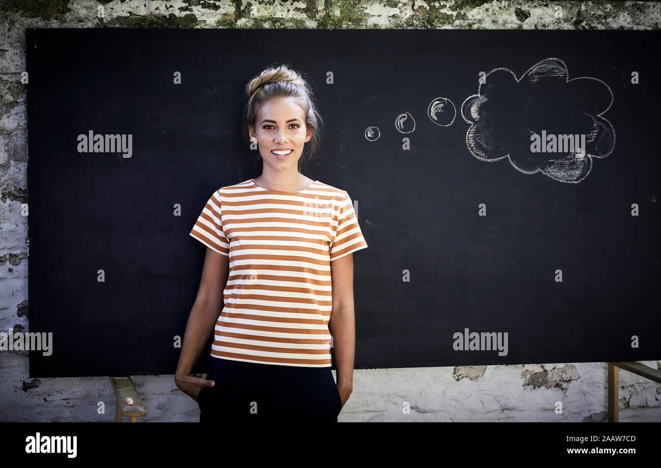 Sorridente giovane donna in piedi di fronte a una lavagna accanto a un fumetto pensiero Foto Stock
