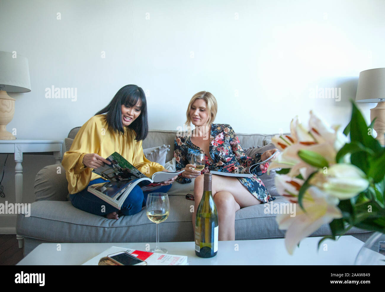 Amici seduti sul divano, lettura di riviste, bere vino Foto Stock