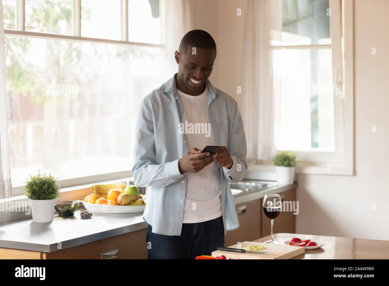 African American uomo utilizzare il cellulare per la cottura in cucina Foto Stock