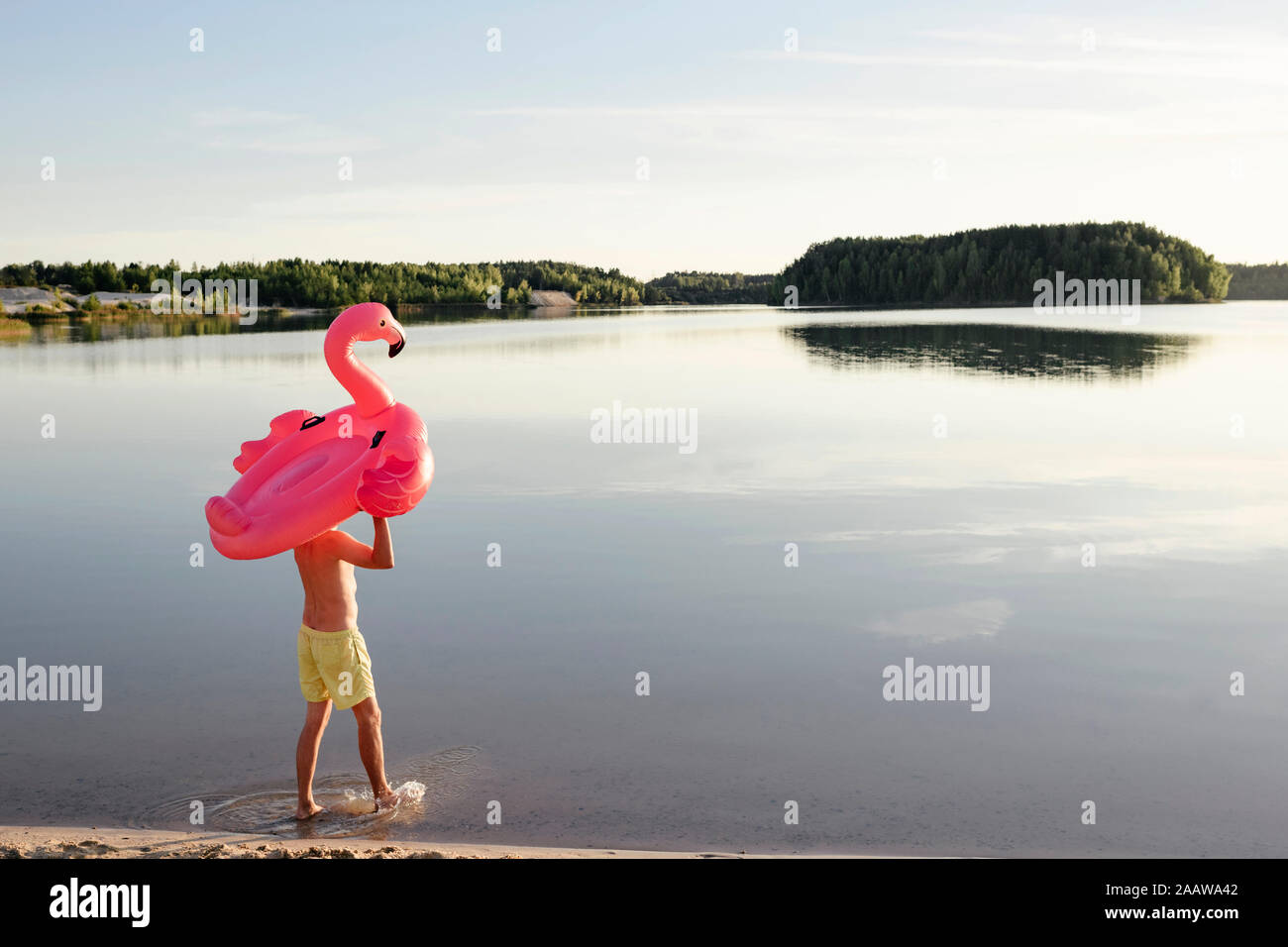 Giovane con flamingo piscina galleggiante camminando sul lungolago Foto Stock