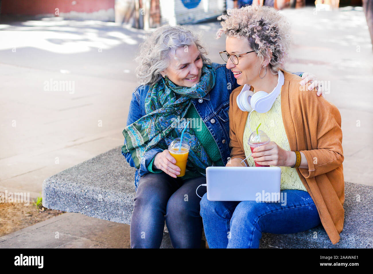 Senior madre con sua figlia adulta utilizzando laptop e bere succhi di frutta in città Foto Stock