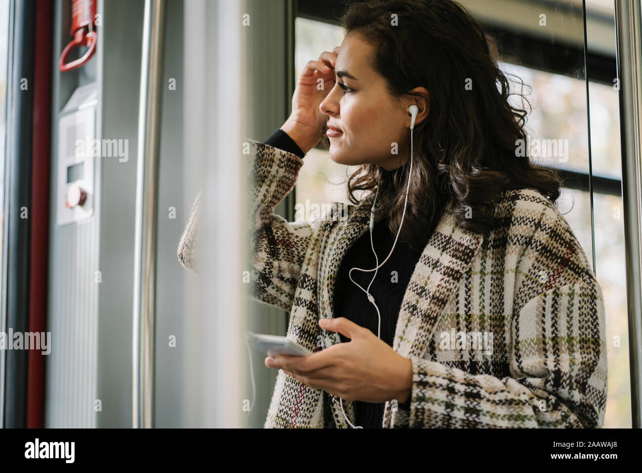 Giovane donna con gli auricolari e lo smartphone su un treno della metropolitana Foto Stock