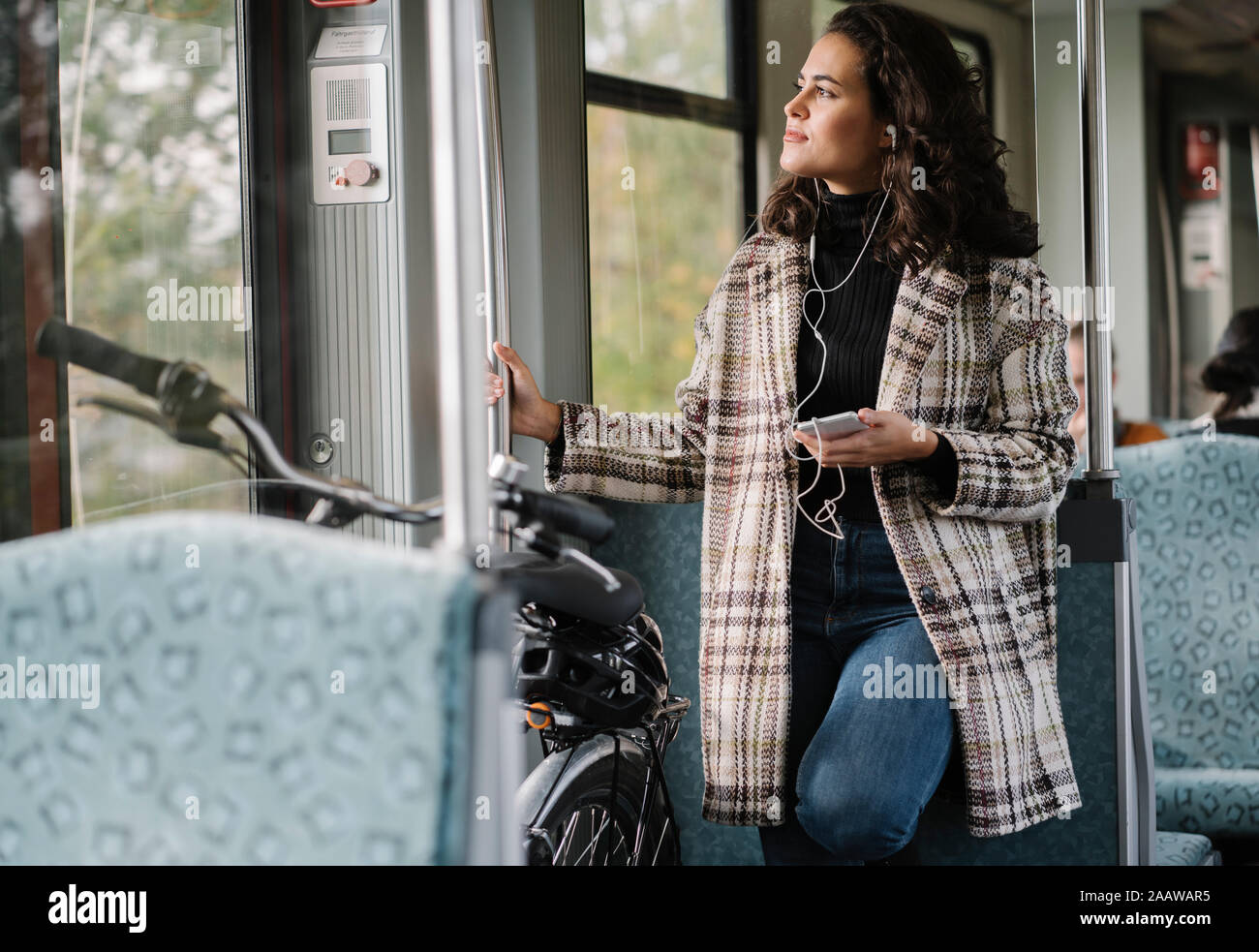 Giovane donna con auricolari, smartphone e bicicletta su un treno della metropolitana Foto Stock