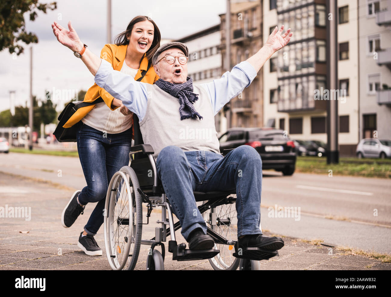 Ritratto di giovane donna spingendo senior uomo in sedia a rotelle su un marciapiede Foto Stock
