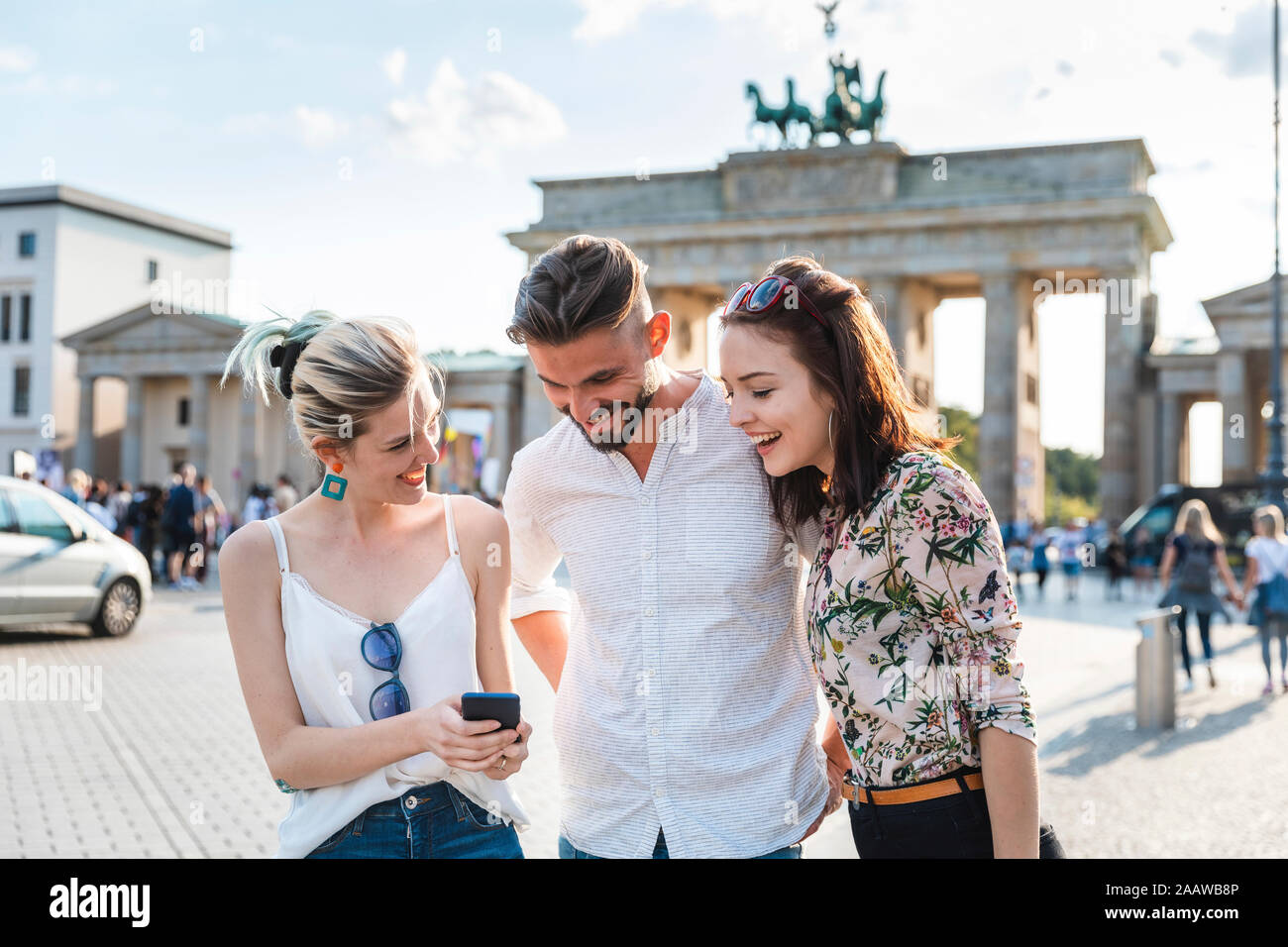 Tre amici guardando il telefono cellulare nella parte anteriore del Brandenburger Tor, Berlino, Germania Foto Stock