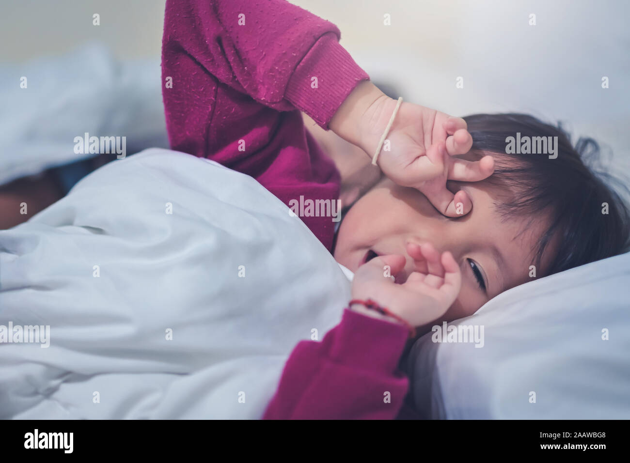 Asian bambina essere assonnato prima di svegliarsi sul letto al mattino tempo in camera da letto Foto Stock