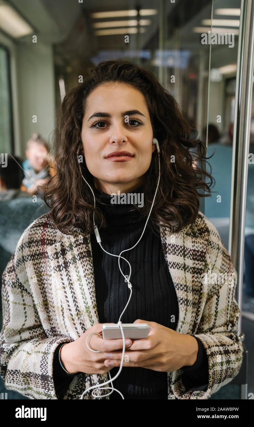 Ritratto di giovane e bella donna con gli auricolari e lo smartphone su un treno della metropolitana Foto Stock