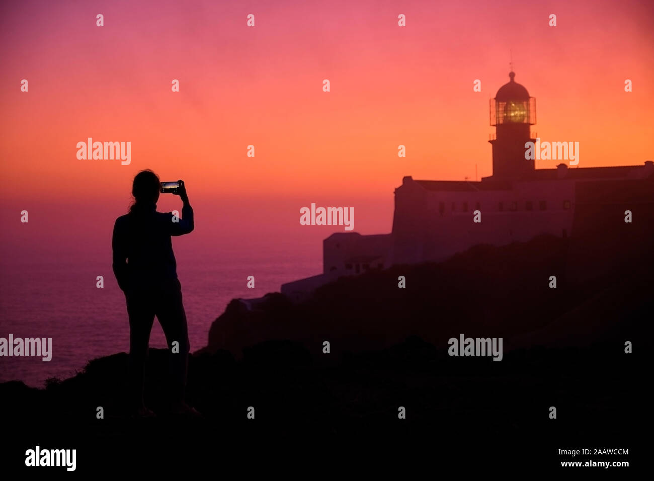Il Portogallo, Algarve, Silhouette della persona tenendo smart phone Foto di Capo San Vincenzo faro all'alba Foto Stock