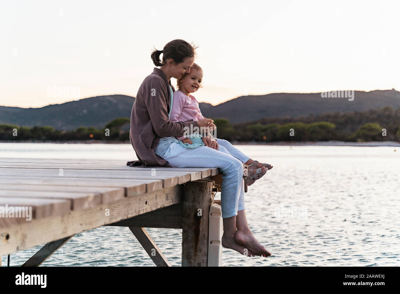 Felice madre con figlia seduto su di un molo al tramonto Foto Stock