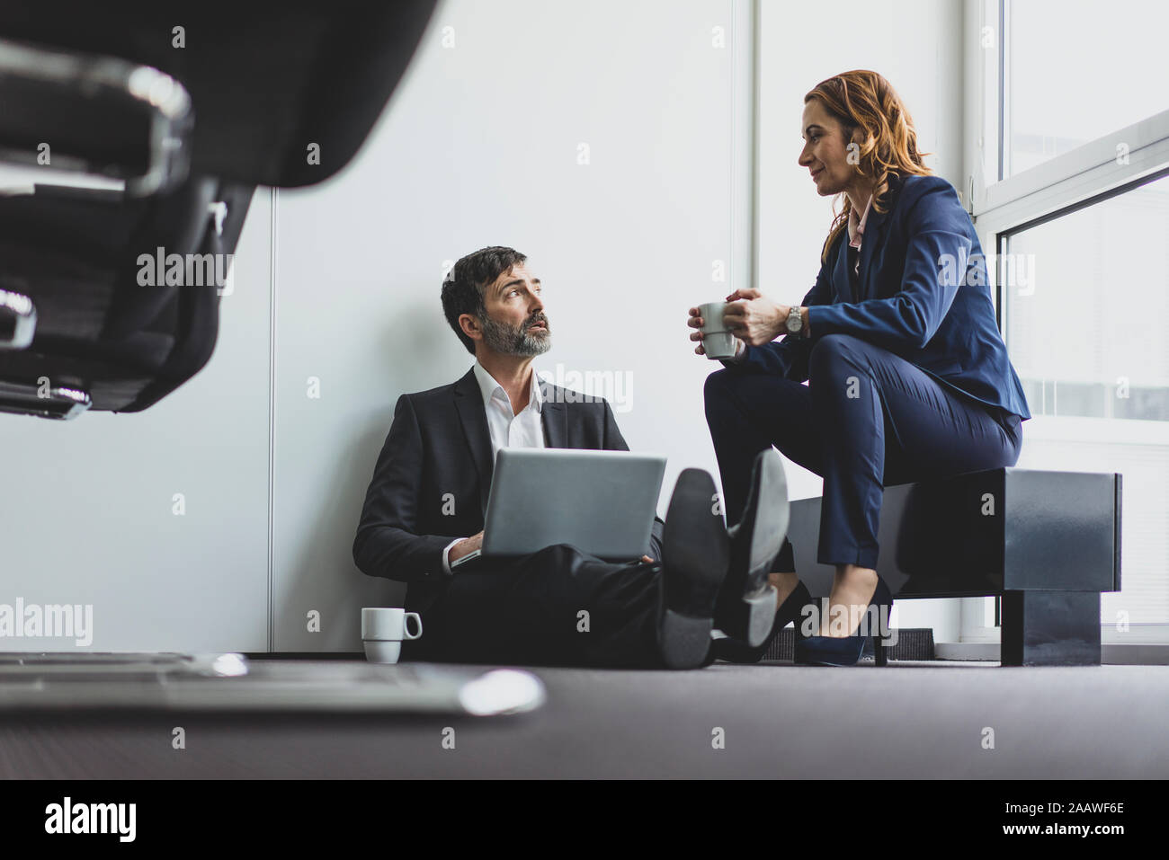 Imprenditrice con imprenditore in ufficio seduti sul pavimento con il computer portatile Foto Stock