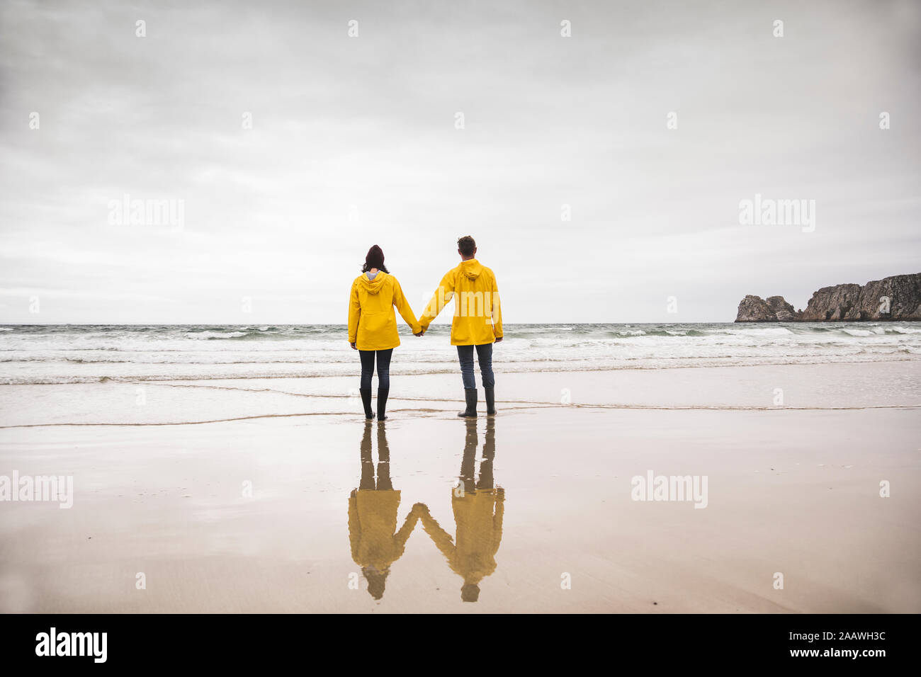 Giovane donna indossa giallo giacche pioggia e di stare in spiaggia, Bretagne, Francia Foto Stock
