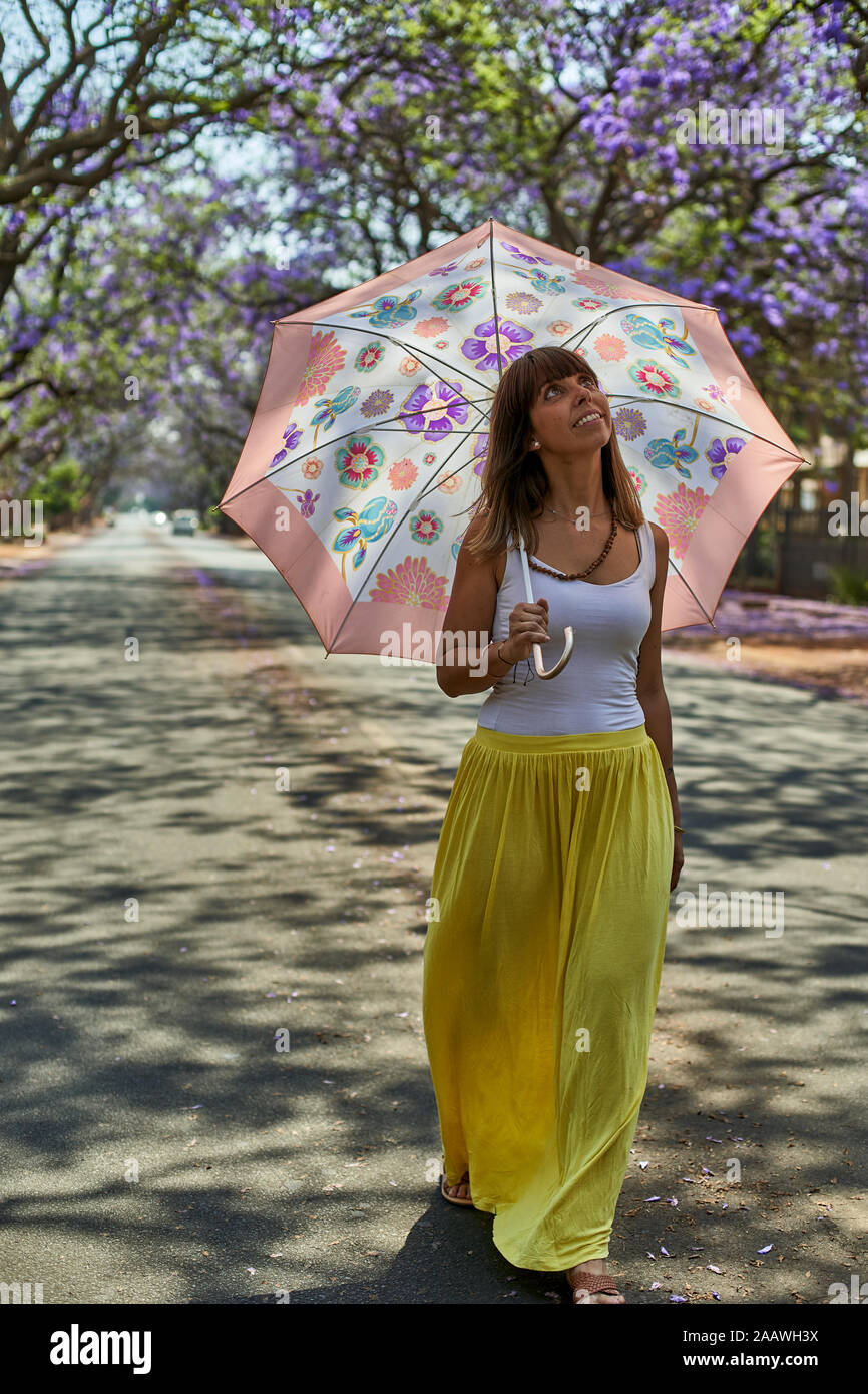 Donna che cammina con il suo ombrello su una strada, alberi di jacaranda in fioritura, Pretoria, Sud Africa Foto Stock