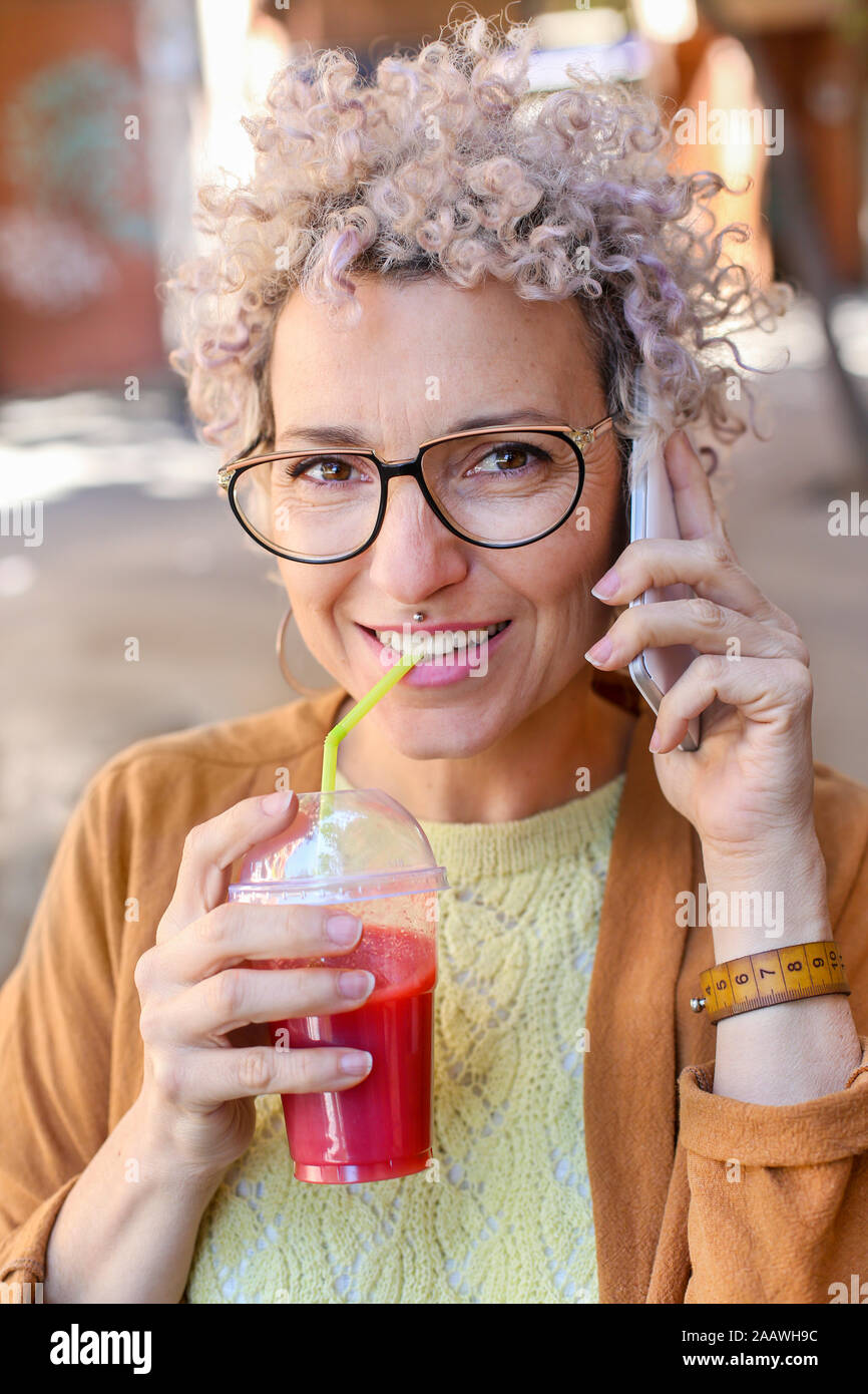Ritratto di una donna che utilizza smartphone e bere un succo di frutta all'aperto Foto Stock