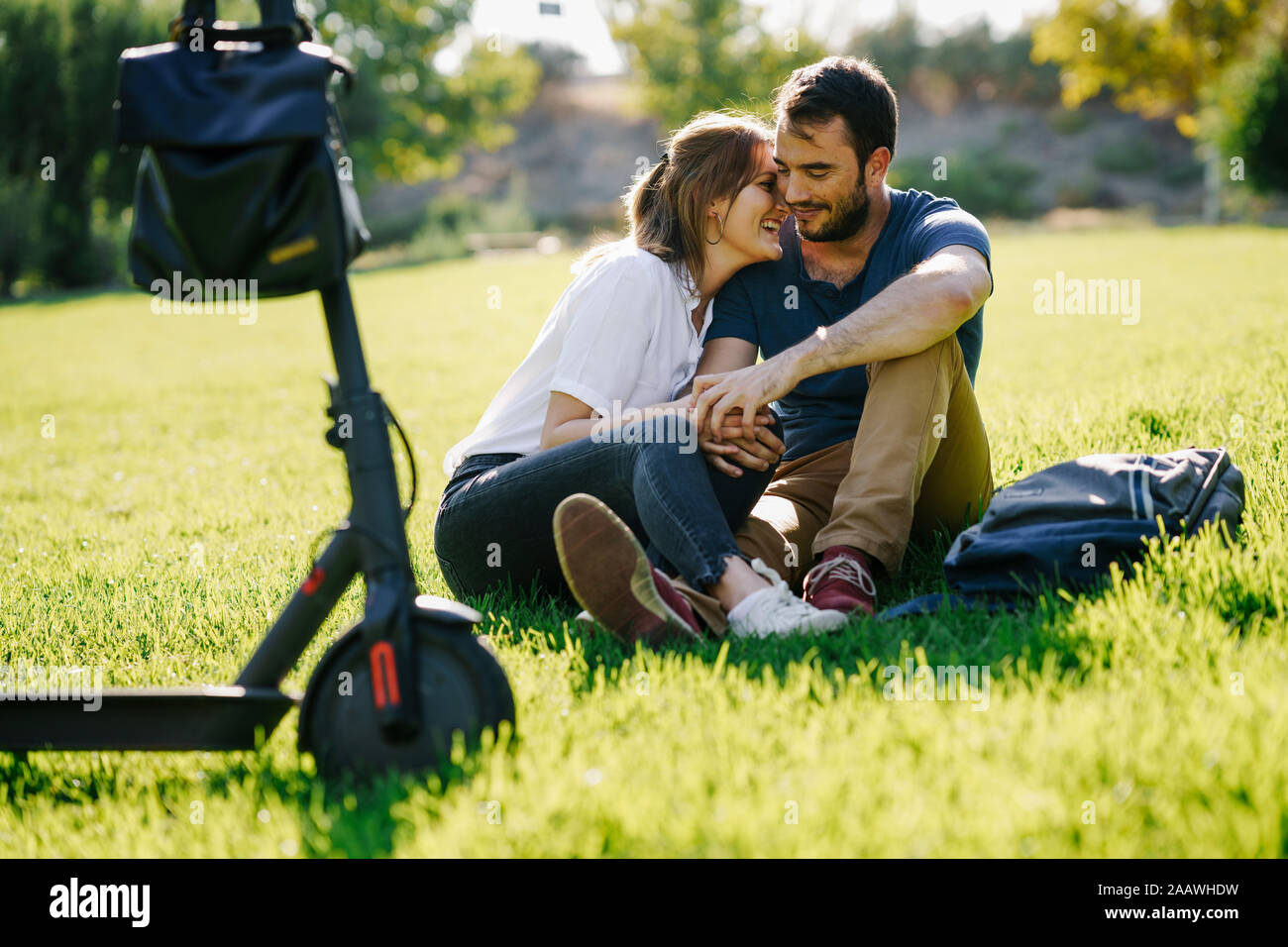 Coppia felice con lo scooter elettrico relax su un prato in un parco Foto Stock