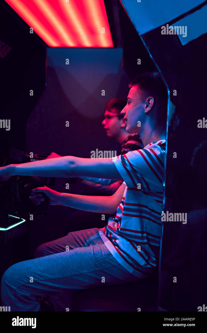 Teenage amici a giocare con un simulatore di guida in una sala giochi Foto Stock