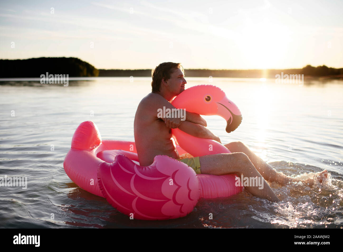 Giovane con flamingo piscina galleggiante sul lago Foto Stock