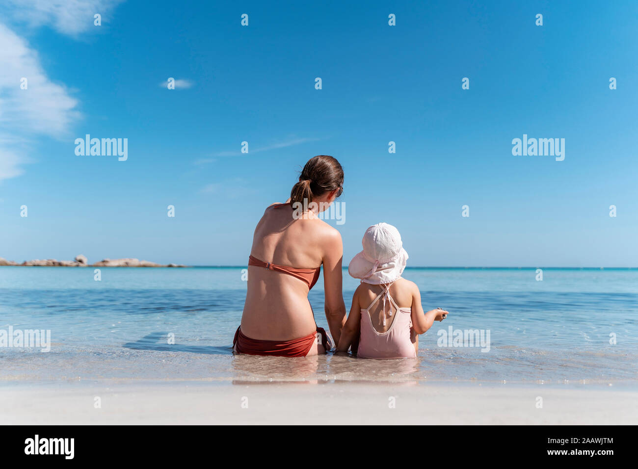 Vista posteriore della madre con la figlia seduta in mare Foto Stock