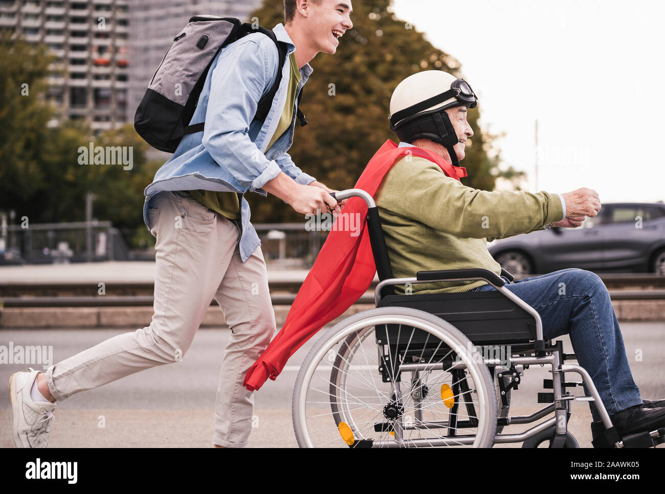 Giovane uomo spingendo senior uomo seduto in una sedia a rotelle vestito come supereroe Foto Stock