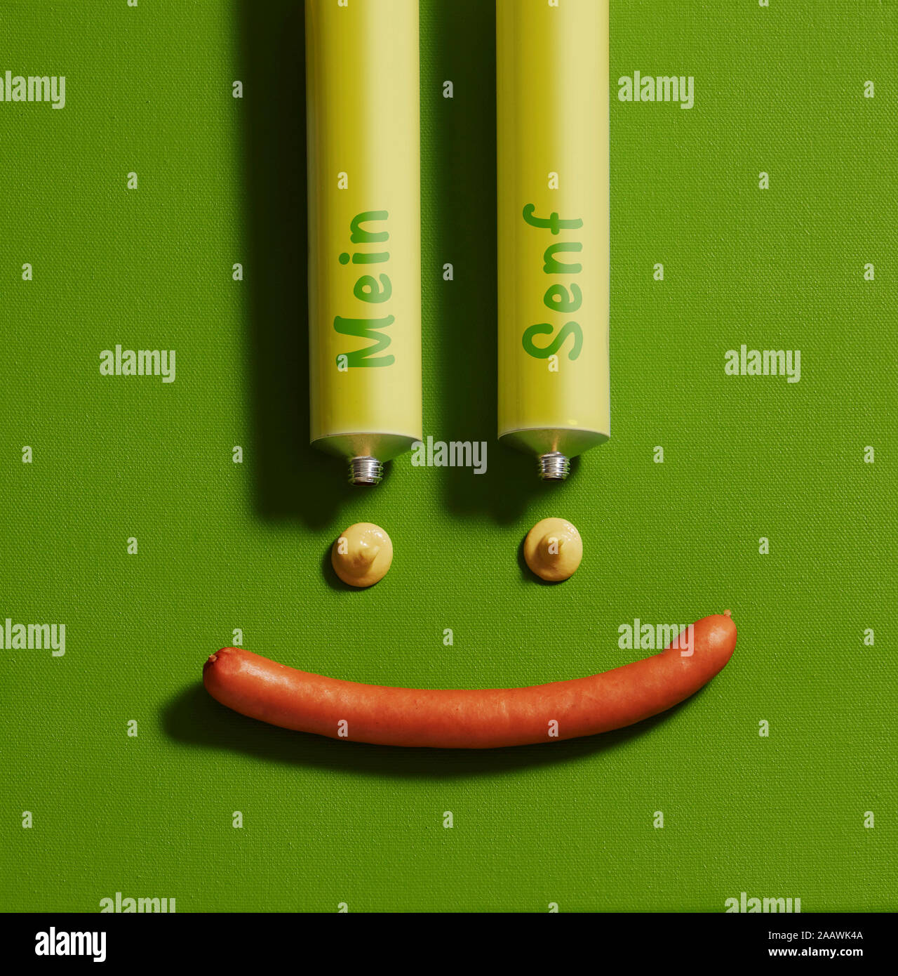 Close-up di antropomorfi Smiley face realizzato con la salsa di senape di tubi e salsicce su tela verde Foto Stock