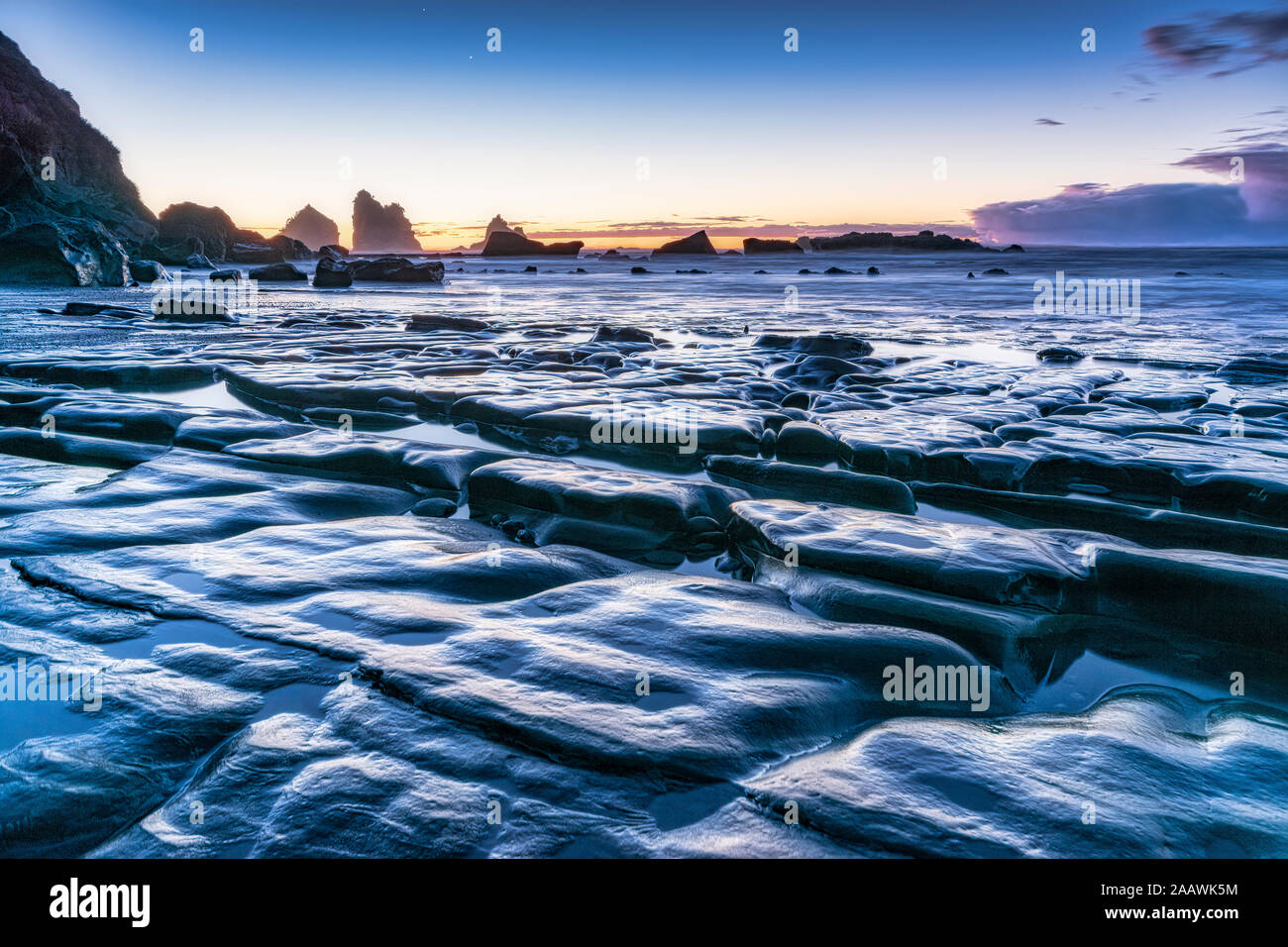 Nuova Zelanda, Sud isola rocciosa costa del mare al tramonto con Motukiekie spiaggia mare pile in distanza Foto Stock