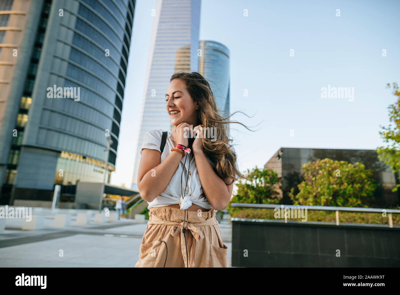 Giovane Donna con cuffie attorno al collo, grattacieli in background Foto Stock