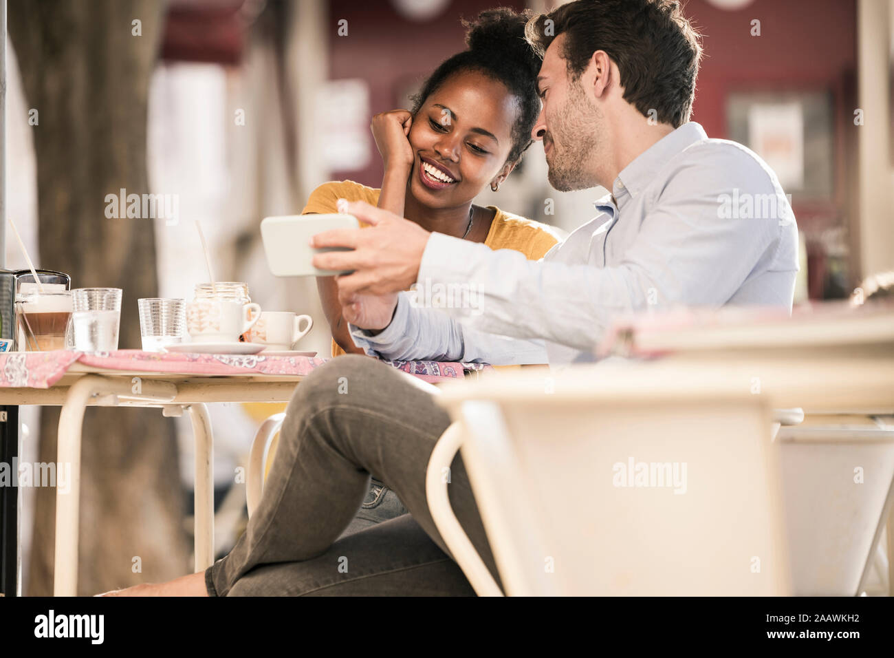 Felice coppia giovane con il telefono cellulare a un cafe' all'aperto Foto Stock