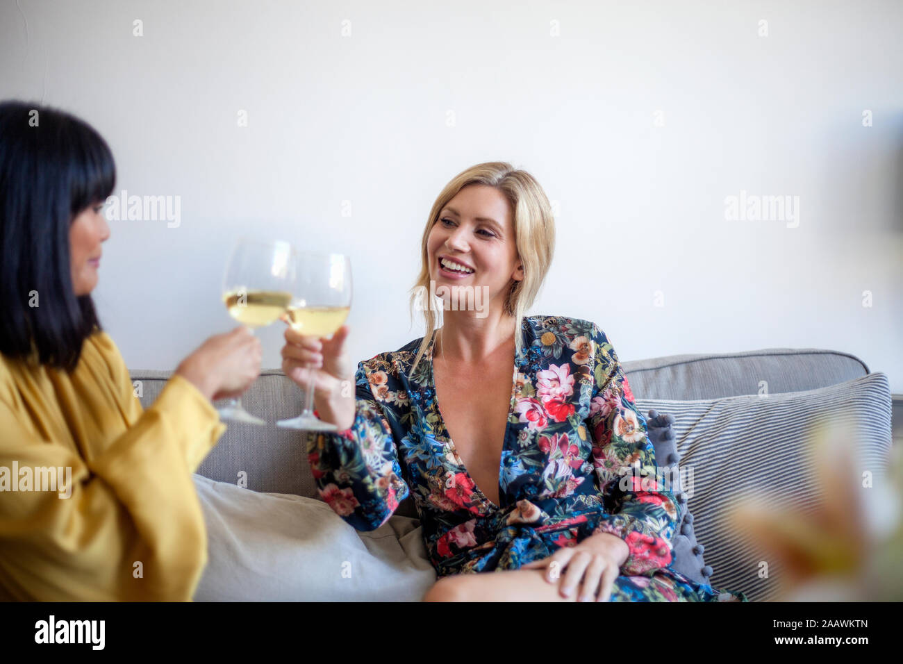 Due amici sittng sul lettino, bere vino, sorridente Foto Stock