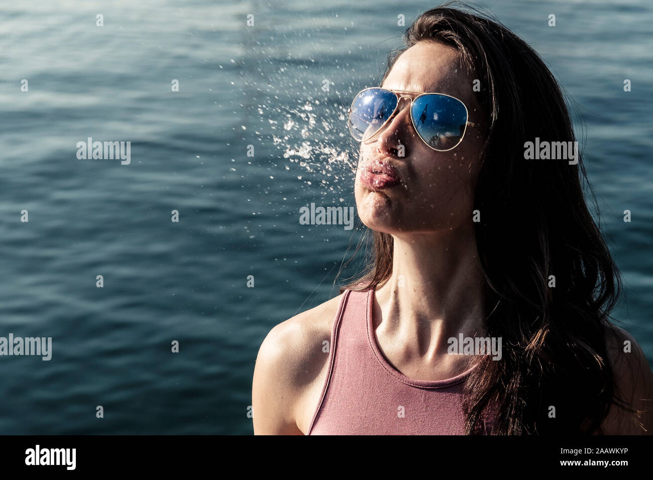 Ritratto di giovane donna che indossa gli occhiali da sole sbuffare acqua Foto Stock
