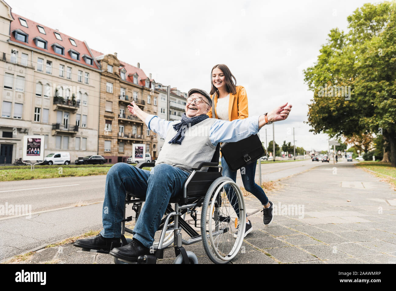 Sorridente giovane donna felice di spinta senior uomo in sedia a rotelle Foto Stock