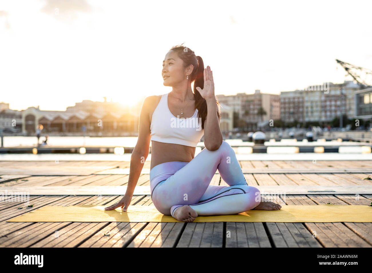 Donna asiatica la pratica dello yoga su un molo a porto, mezza torsione spinale al tramonto Foto Stock