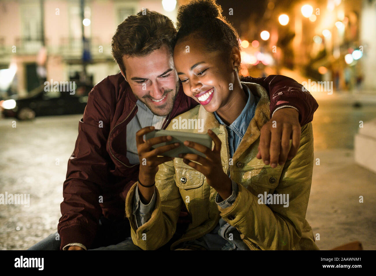 Ritratto di felice coppia giovane guardando insieme a smartphone di notte, Lisbona, Portogallo Foto Stock
