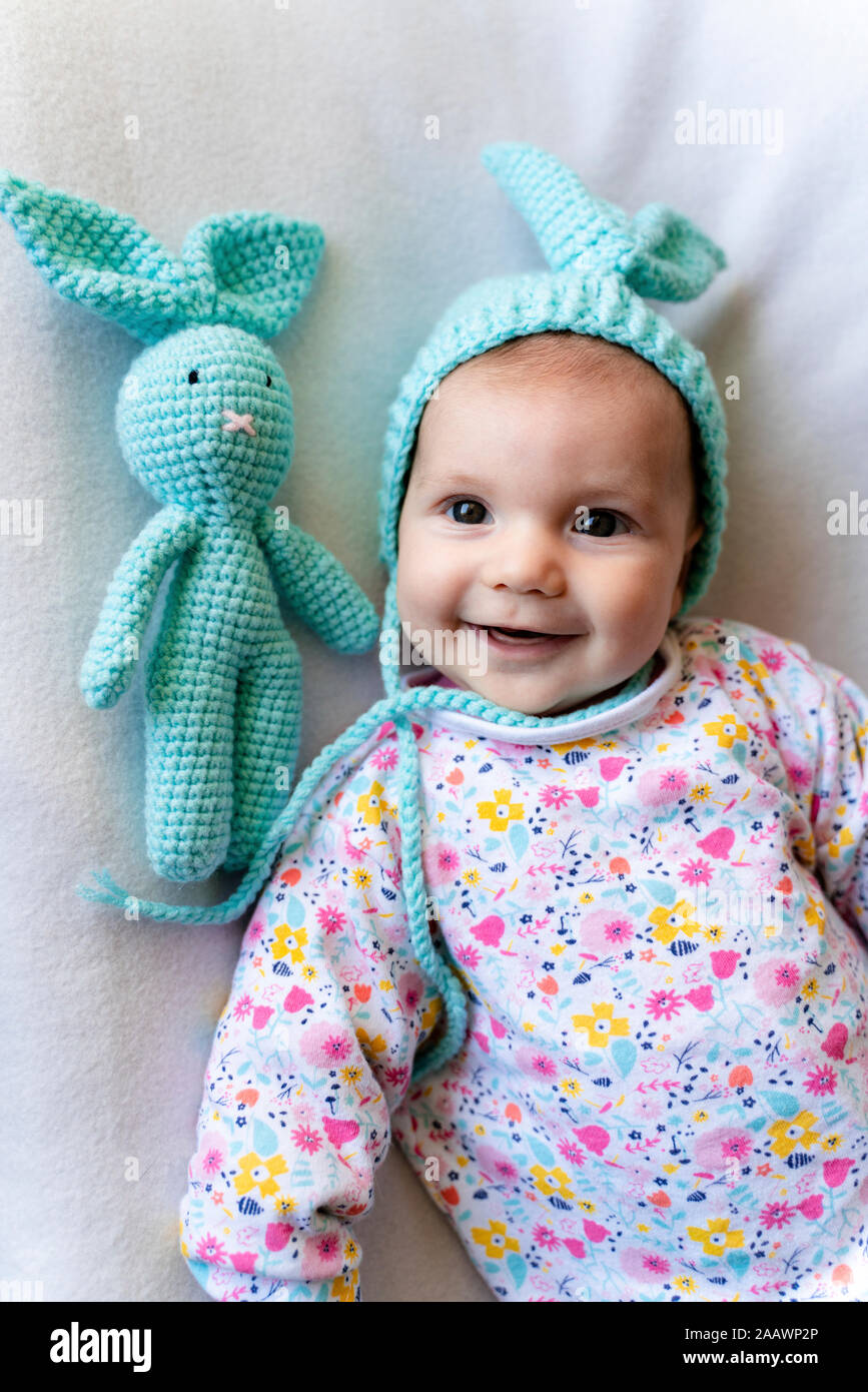Bambina con bunny hat e un coniglietto toy giacente sul letto Foto Stock