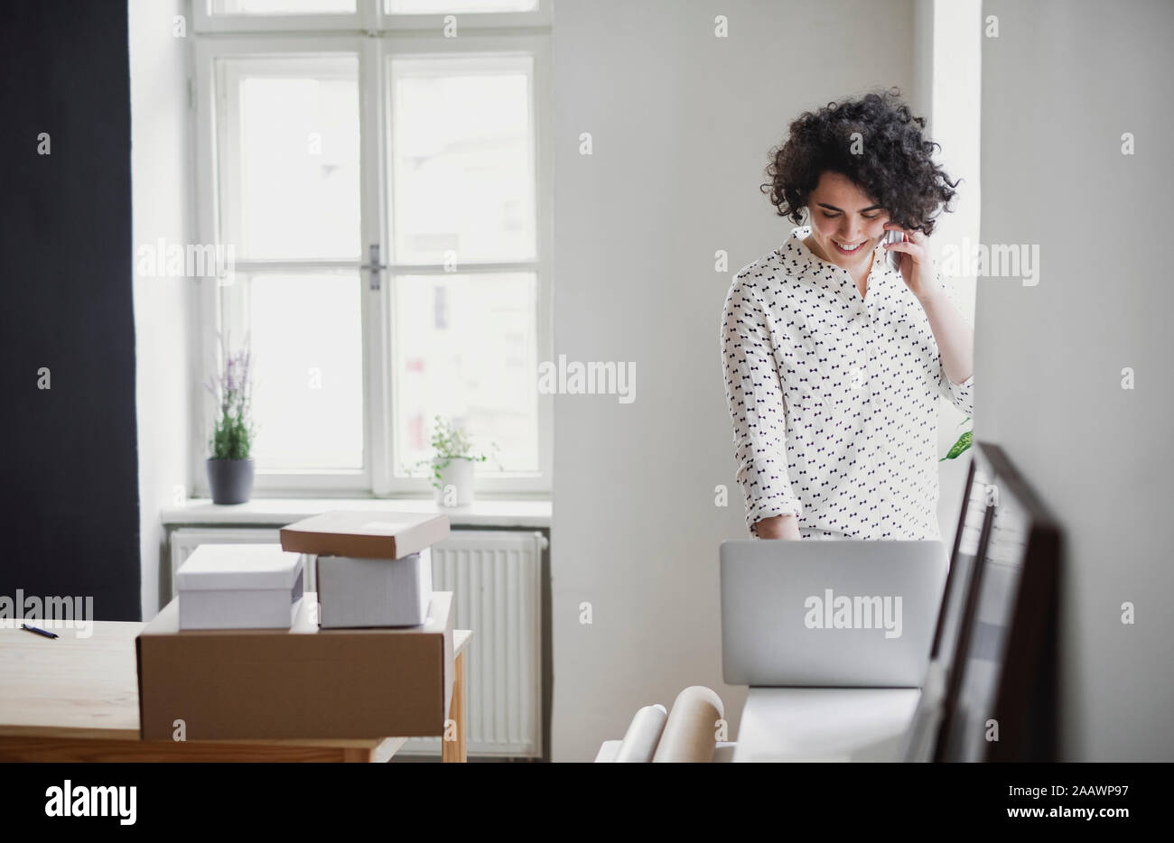 Sorridente giovane donna sul telefono cellulare utilizzando il computer portatile in ufficio in casa Foto Stock