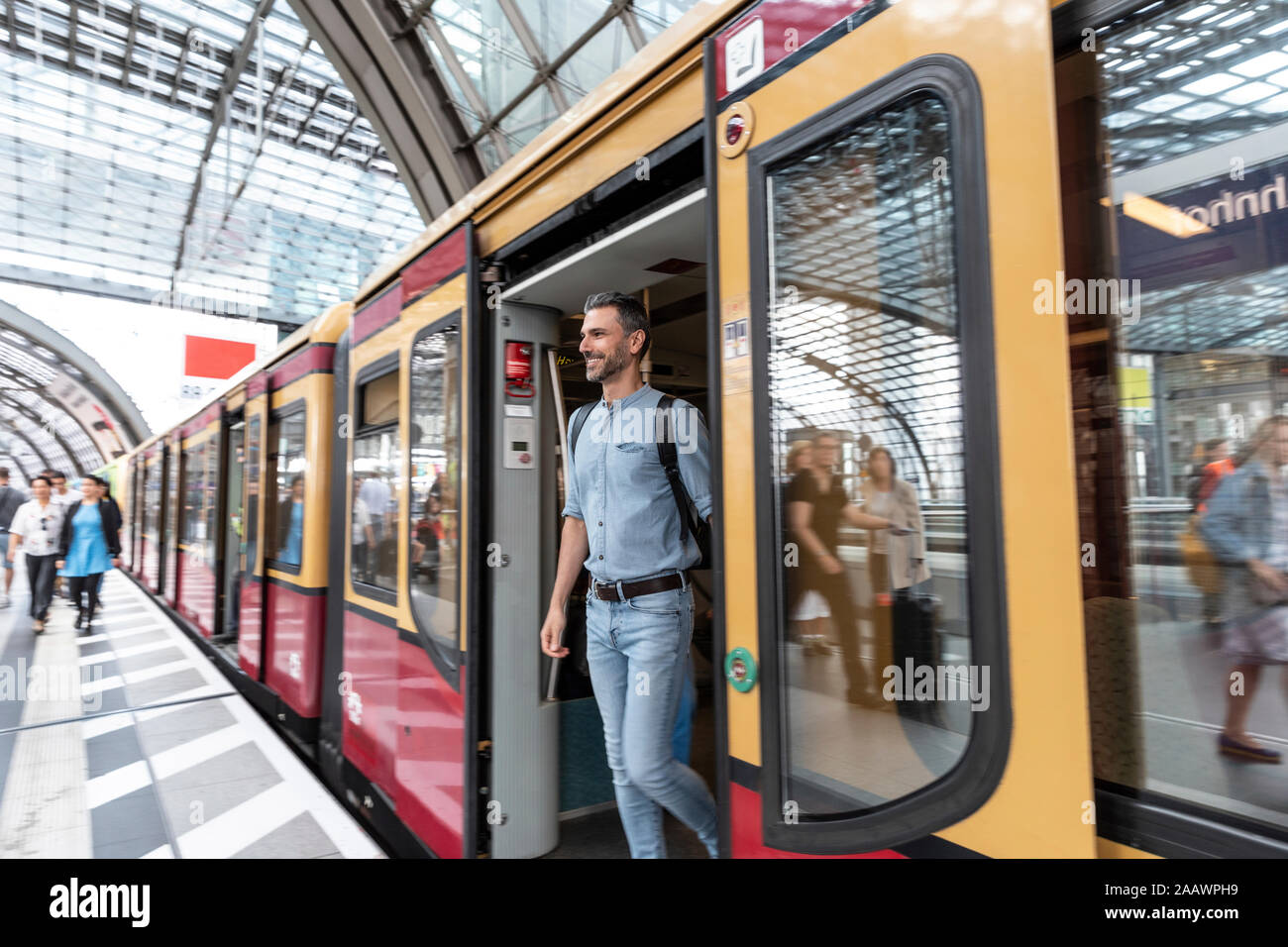Uomo sorridente che esce dal treno alla piattaforma della stazione, Berlino, Germania Foto Stock