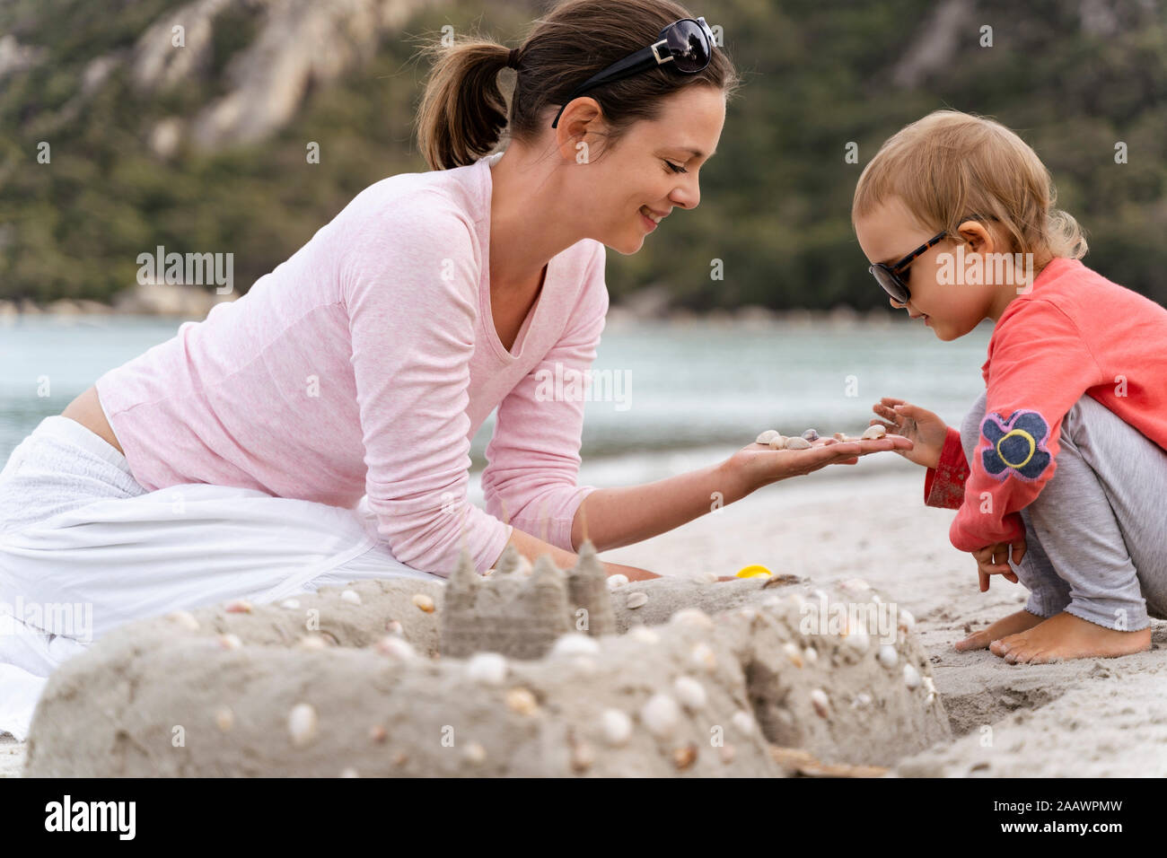 Felice madre e figlia e la costruzione di un castello di sabbia sulla spiaggia Foto Stock