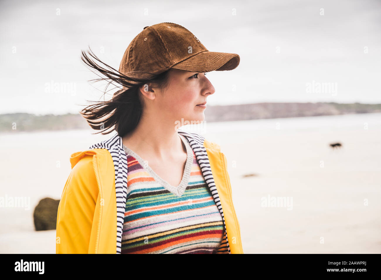 Ritratto di giovane donna che indossa giallo Giacca pioggia in spiaggia, Bretagne, Francia Foto Stock