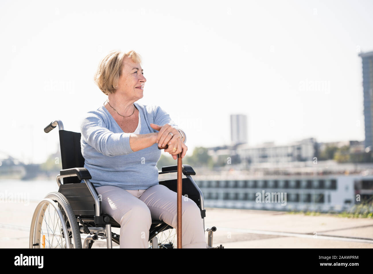 Senior donna seduta in sedia a rotelle, con bastone Foto Stock
