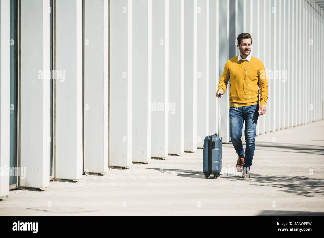 Giovane Uomo con valigia scorrevole e gli auricolari nella città sul go Foto Stock